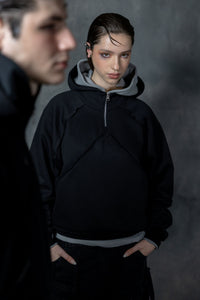 Two people wearing dark hoodies against a gray background
