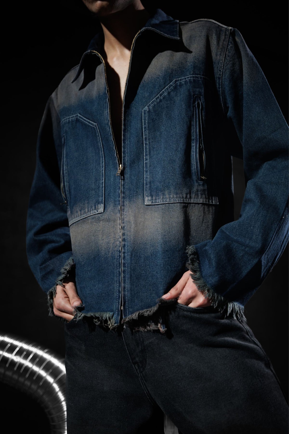 Close-up of a blue denim jacket with zipper closure and frayed edges, highlighting modern streetwear design