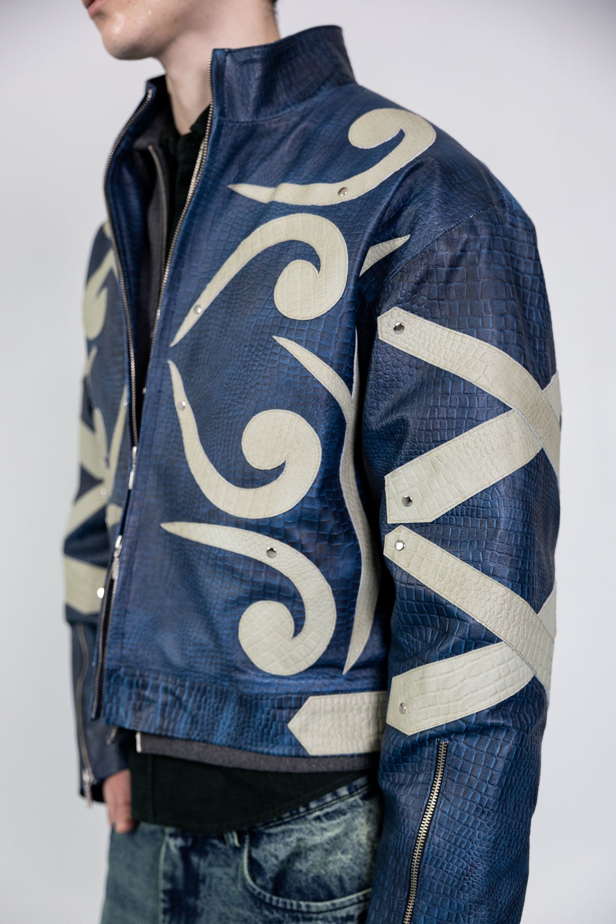 Angled view of men's blue embossed leather jacket with beige appliqué details