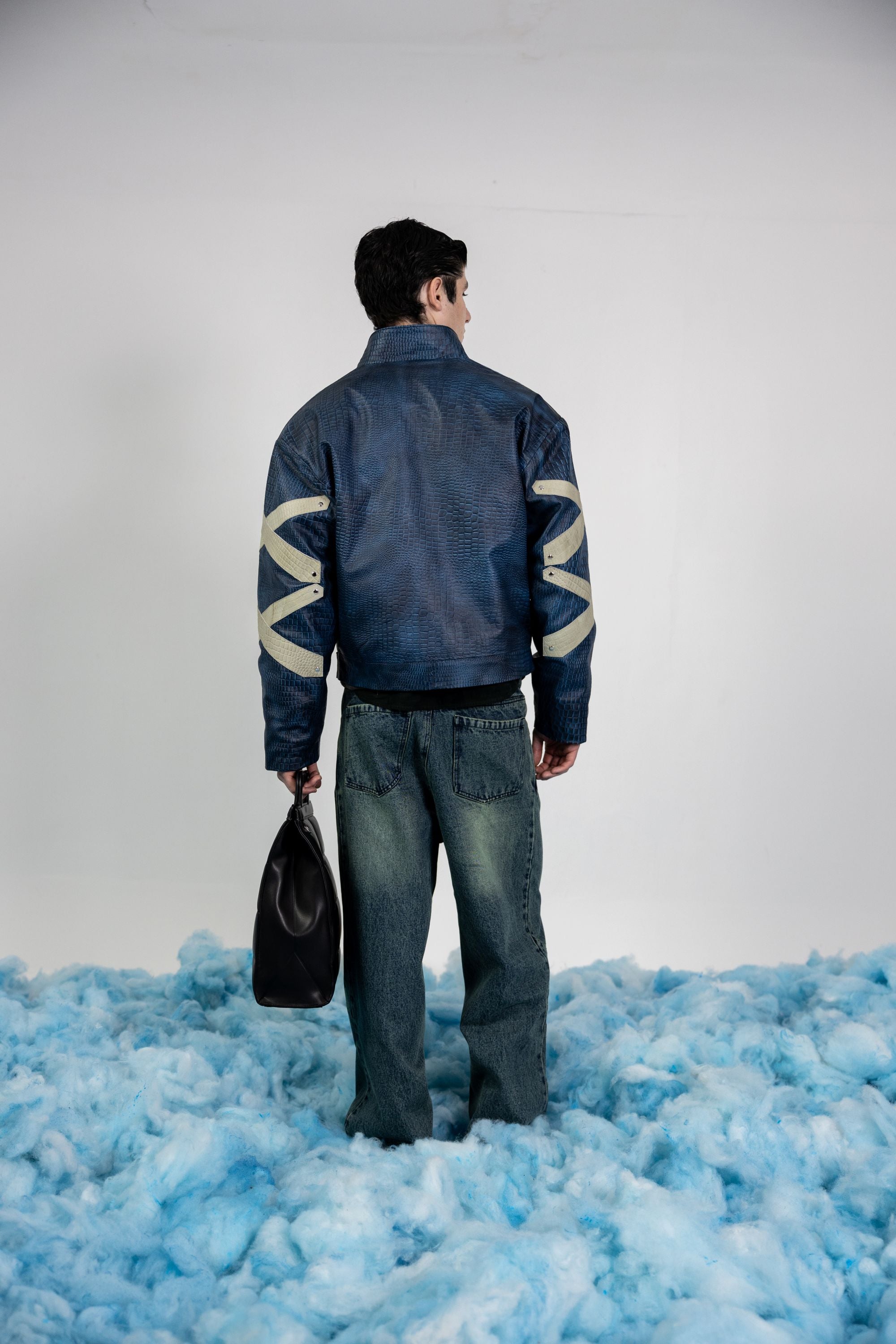 Back view of men's blue embossed leather jacket featuring abstract beige appliqué patterns and metal rivets
