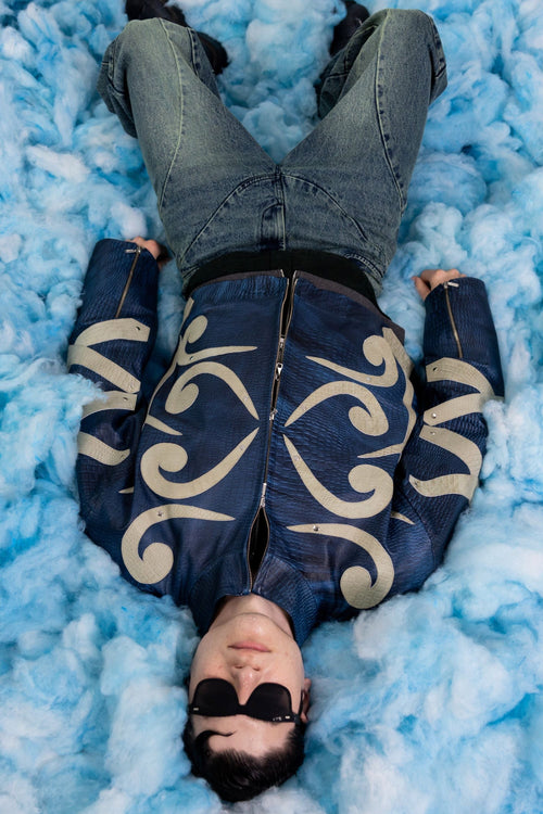 Flat lay view of blue embossed leather jacket with beige appliqué