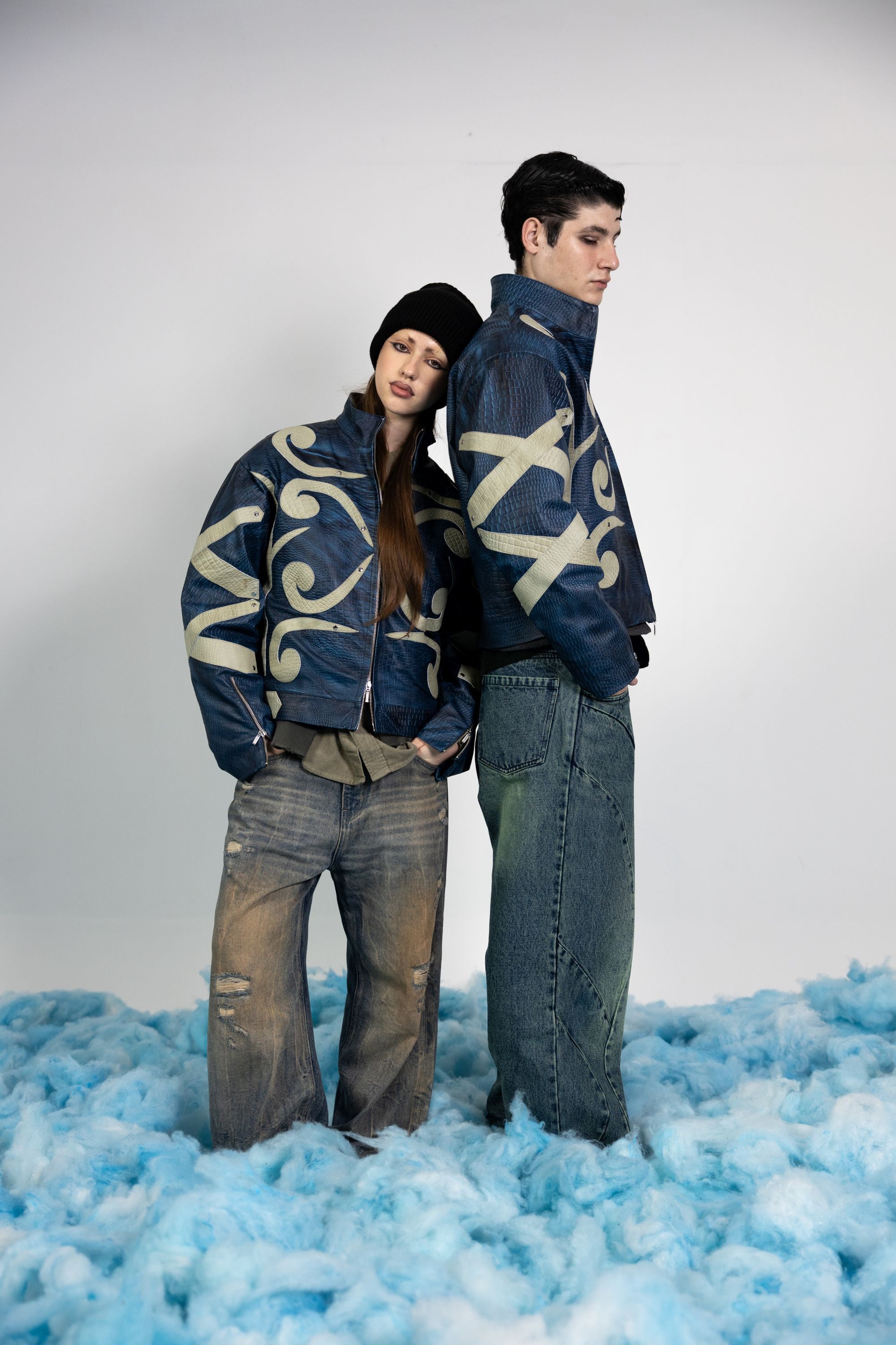 Couple wearing matching premium blue embossed leather jackets with beige appliqué designs, styled for a modern streetwear look