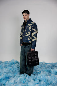 Front view of men's blue crocodile-embossed leather jacket featuring contrasting beige abstract appliqué designs and metal rivets