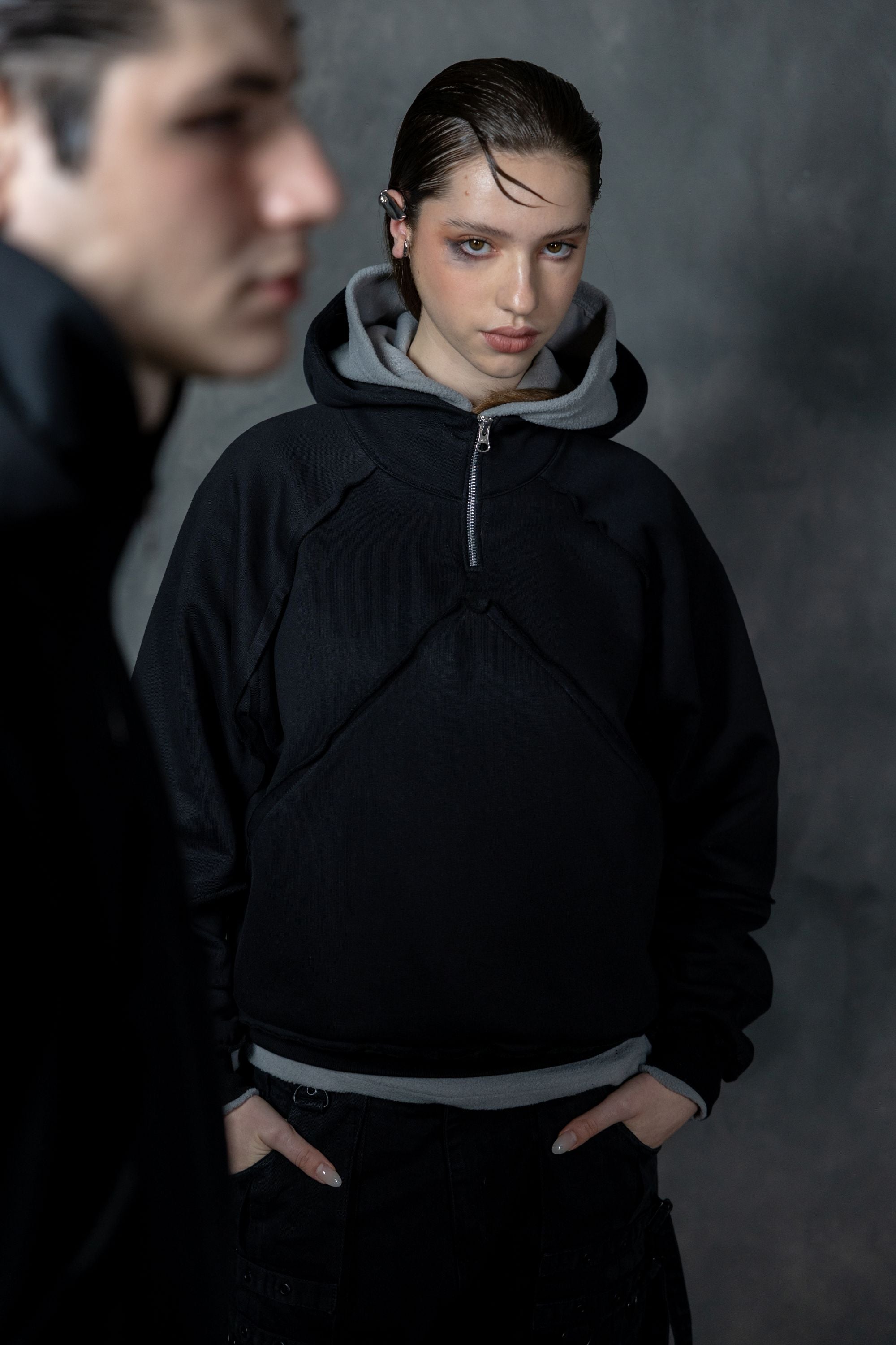 Woman wearing a premium black zip hoodie with a unique layered hood design, minimal modern streetwear style